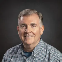 A man with light skin tone and gray hair in a blue plaid shirt
