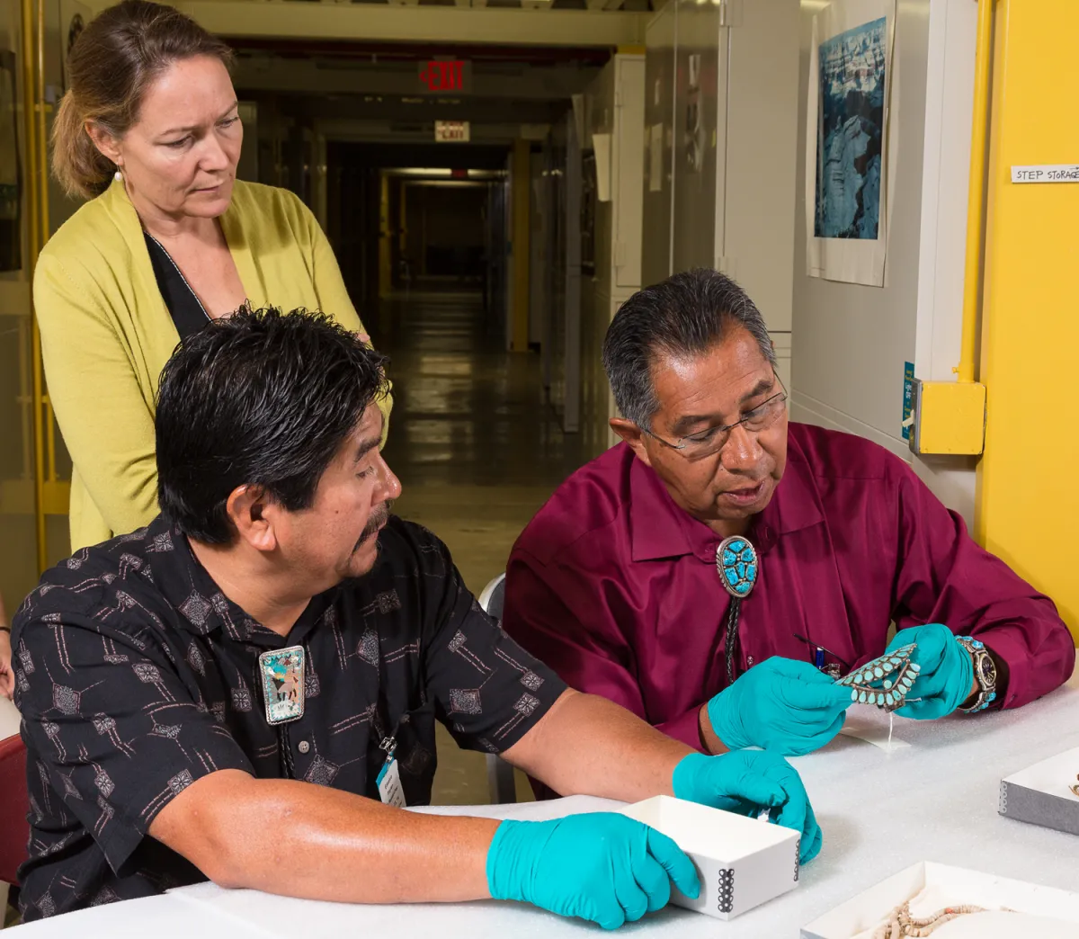 Curator and two men in storage area looking at turquoise jewelry